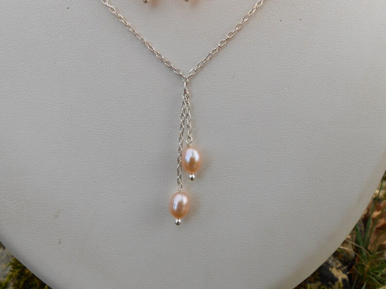 May include: A silver chain necklace with a delicate drop featuring two blush-colored pearls.