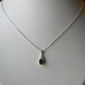 May include: A silver chain necklace with a small oval-shaped black gemstone pendant.