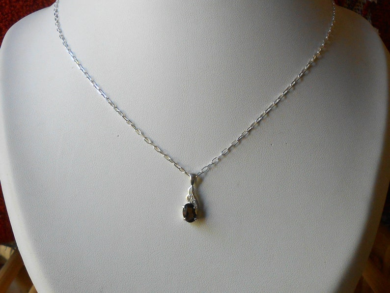 May include: A silver chain necklace with a small oval-shaped black gemstone pendant.