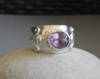 May include: A silver ring with an ornate design and a large, round, purple amethyst gemstone.