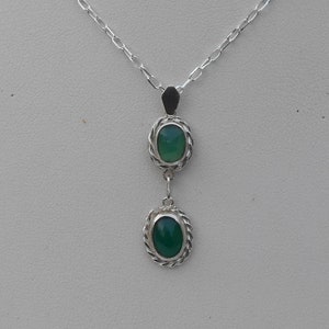 May include: A silver necklace with a pendant featuring two green oval stones set in silver.