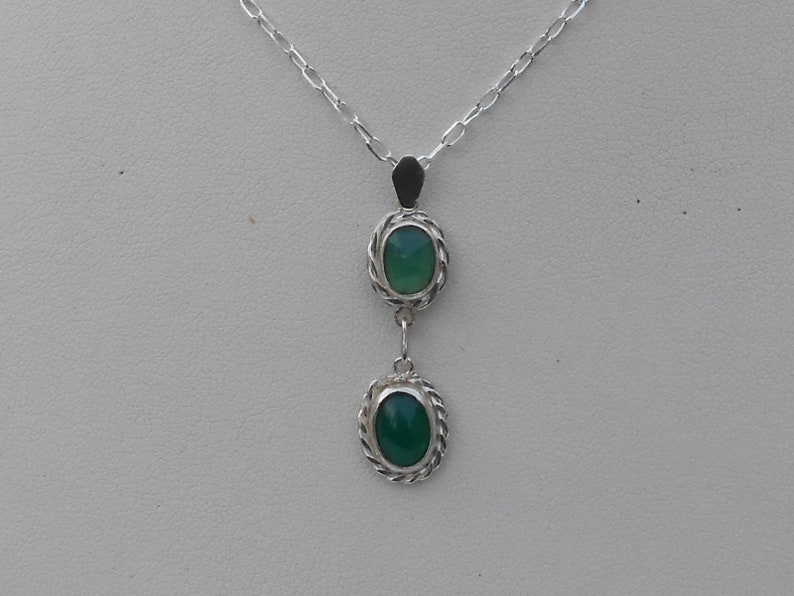 May include: A silver necklace with a pendant featuring two green oval stones set in silver.