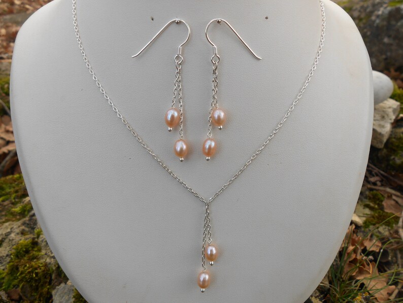 May include: A silver necklace and earrings set with a delicate chain and three pink pearls dangling from each piece.