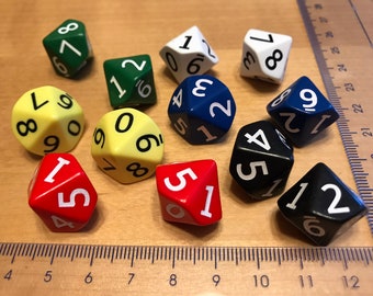 May include: A collection of ten multi-sided polyhedral dice in various colors including red, yellow, green, white, blue, and black, each featuring white or black printed numbers, arranged next to a clear plastic ruler showing centimeter markings.