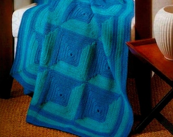 May include: A crocheted throw blanket in shades of teal and blue with a square pattern. The blanket is draped over a white armchair.