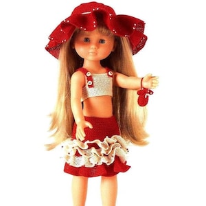 Peut inclure: Une tenue de poupée en crochet rouge et blanc avec un chapeau assorti. La poupée porte des chaussures rouges et a de longs cheveux blonds.