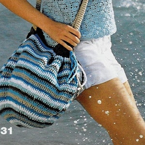 Puede incluir: Bolso de crochet a rayas azules, blancas y beige, con cierre de cordón y correa beige. El bolso lo lleva una persona con un top azul y pantalones cortos blancos. El número 31 es visible en la esquina inferior izquierda.