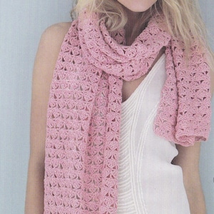 Può includere: Una sciarpa rosa all'uncinetto con un delicato motivo traforato. La sciarpa è drappeggiata intorno al collo di una persona che indossa una canotta bianca.