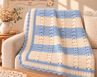 May include: A crochet blanket featuring alternating horizontal stripes of light blue and cream yarn. The blanket has a textured openwork pattern and a scalloped light blue border. The text Le crochet de Anne is visible above.