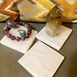 May include: Three white selenite charging plates with a purple amethyst bracelet, a turquoise ring, and a clear smoky quartz crystal on top.