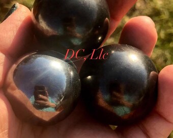May include: Three black obsidian spheres, polished to a high shine, reflecting light in a hand.
