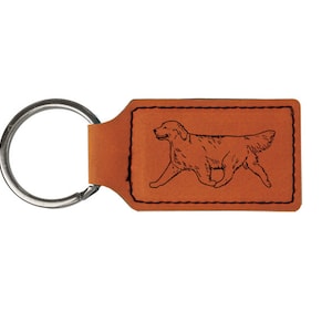 May include: A brown leather keychain with a silver key ring and a black line drawing of a golden retriever running on a tan background.