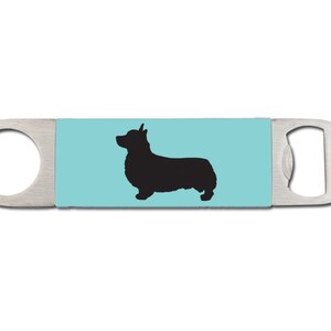 May include: A silver bottle opener with a blue background and a black silhouette of a corgi.