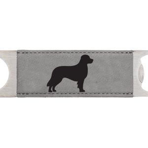 May include: A silver bottle opener with a gray leatherette insert featuring a black silhouette of a dog.