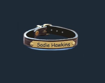 May include: A brown leather dog collar with a gold-colored buckle and nameplate. The nameplate reads "Sadie Hawkins" in a simple, sans-serif font. The collar is dark brown and has a classic design.