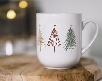 May include: White ceramic mug with a Christmas tree design. The trees are drawn in a simple style with red, green, and gold accents.