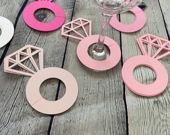 May include: Pink and white ring-shaped wine glass charms with a diamond design. The charms are made of cardboard and are perfect for a bridal shower or bachelorette party.