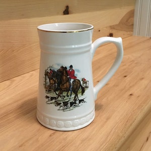 May include: White ceramic mug with a gold rim and a hunting scene featuring riders on horseback and hounds. The scene is printed on the front of the mug.