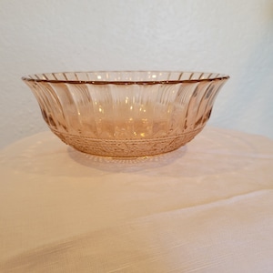 May include: A clear, pink glass bowl with a scalloped rim and a decorative pattern. The bowl is sitting on a white surface.