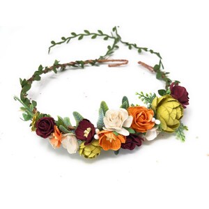 May include: A floral crown with burgundy, orange, yellow, and white paper flowers. The crown is made with a brown wire base and green leaves.