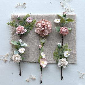 May include: Five pink and white floral hair clips with green leaves. The clips are made of fabric and have a delicate, feminine look.