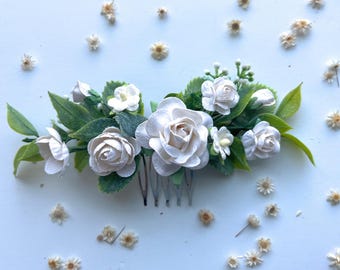 Puede incluir: Un peine para el cabello floral blanco con un grupo de flores de papel blanco y hojas verdes. El peine tiene una base de metal plateado.