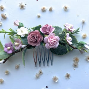 May include: A pink and white floral hair comb with a silver comb. The comb is decorated with small pink and white flowers and green leaves.