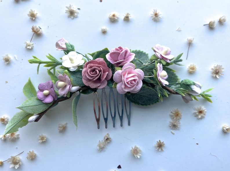May include: A pink and white floral hair comb with a silver comb. The comb is decorated with small pink and white flowers and green leaves.