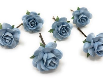 Puede incluir: Seis pinzas para el pelo de flores de papel azul claro con hojas verdes. Las flores están dispuestas en círculo sobre un fondo blanco.