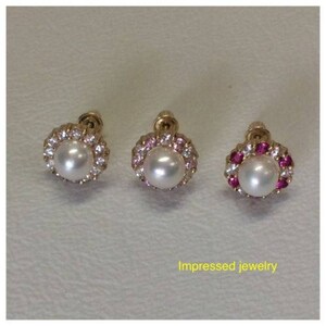 Op de afbeelding: Drie paar gouden oorbellen met een parel in het midden en een halo van kleine steentjes. De oorbellen links hebben heldere steentjes, de oorbellen in het midden hebben roze steentjes en de oorbellen rechts hebben rode steentjes.