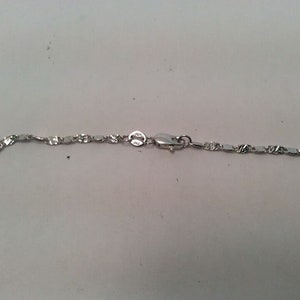 May include: A silver chain necklace with a lobster clasp. The chain is made of small, flat, oval links.