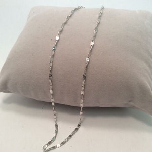 May include: A silver chain necklace with a delicate, textured, square-shaped link design.