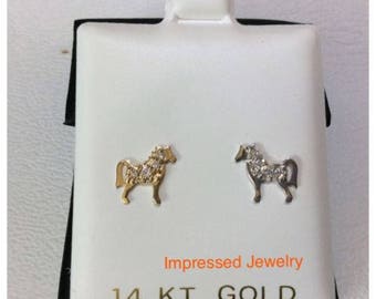 May include: A pair of gold horse stud earrings with clear cubic zirconia stones. The earrings are displayed on a white background with the text "Impressed Jewelry 14 KT. GOLD".