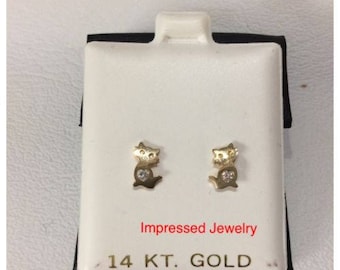 May include: A pair of 14 karat gold cat earrings with a single diamond in the center of each cat. The earrings are displayed on a white card with the text "Impressed Jewelry" and "14 KT. GOLD".