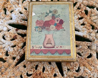 May include: A rectangular framed print featuring a bouquet of flowers in a vase. The flowers are in shades of red, pink, and white. The frame is gold-colored, and the background has a faded, vintage aesthetic.