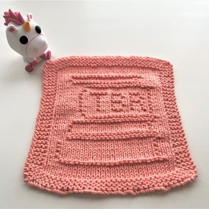 May include: A pink knitted dishcloth with a square pattern in the center. The dishcloth is on a white surface.