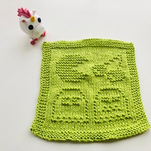 May include: A green knitted dishcloth with a simple design of two squares. The dishcloth is made with a textured stitch.