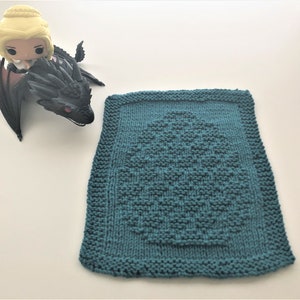 May include: A teal blue knitted dishcloth with a textured design in the center. The dishcloth is square and has a border around the edges.