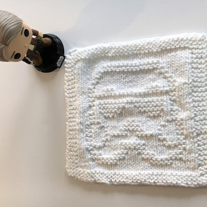 May include: White knitted dishcloth with a raised design. The design is a geometric pattern with a square in the center.