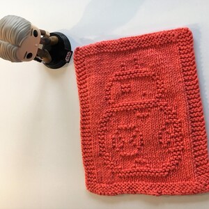 May include: A coral-colored knitted dishcloth with a geometric design. The dishcloth is made of cotton yarn and is perfect for drying dishes or cleaning surfaces.