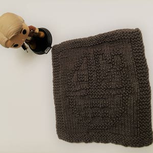 May include: A brown knitted dishcloth with a textured pattern. The dishcloth is square shaped and has a fringe border.