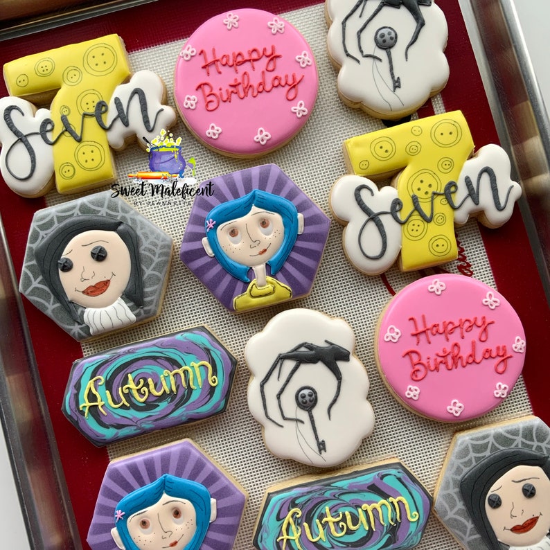 May include: A collection of decorated sugar cookies featuring the characters from the movie "Coraline" and the words "Happy Birthday" and "Autumn". The cookies are decorated with various colors and designs, including a spider, a key, and a swirl pattern.