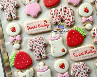 May include: A set of 14 decorated sugar cookies featuring a strawberry theme. The cookies are decorated with pink, red, white, and green icing. The cookies include a baby bottle, a rattle, a onesie, and a banner that says "Sweet Baby is on the way".