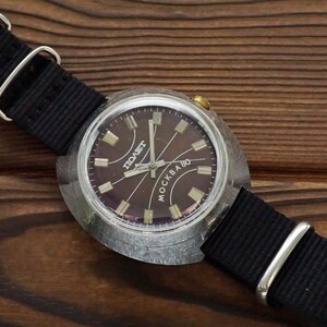 Pode incluir: Um rel&oacute;gio de pulso prateado com um mostrador preto e uma pulseira preta. O mostrador do rel&oacute;gio tem as palavras "СОВЕТ" e "МОСКВА 80" impressas nele.