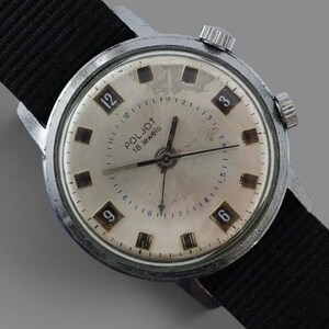 Op de afbeelding: Een vintage Poljot polshorloge met een ronde zilverkleurige kast en een crèmekleurige wijzerplaat. Het horloge heeft zwarte uurmarkeringen, zilveren wijzers en de tekst Poljot 18 Jewels. Het is bevestigd aan een zwarte nylon band met zilverkleurige hardware.