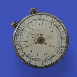 Peut inclure: Une règle à calcul circulaire vintage avec un cadran crème et des marquages noirs. Le corps est en métal et comporte deux boutons de réglage. Le cadran affiche des chiffres et des échelles, avec le texte "Super Spica".