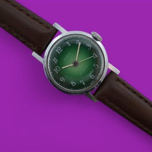 Könnte beinhalten: Eine silberne Armbanduhr mit grünem Zifferblatt und schwarzen Zahlen. Die Uhr hat ein braunes Lederarmband.