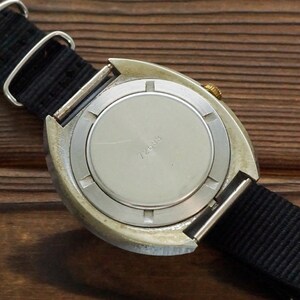 Pode incluir: A parte de tr&aacute;s de um rel&oacute;gio de pulso prateado com uma pulseira de nylon preta. O mostrador do rel&oacute;gio tem uma caixa de metal prateada com uma coroa dourada. O mostrador do rel&oacute;gio tem o texto "724018" impresso nele.