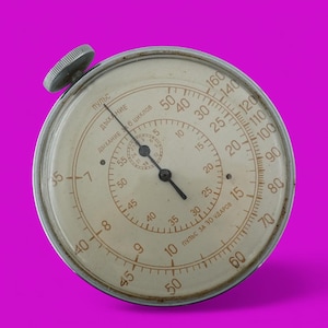 Könnte beinhalten: Vintage Stoppuhr mit cremefarbenem Zifferblatt und schwarzen Zeigern, vor magentafarbenem Hintergrund. Die Stoppuhr hat ein kreisförmiges Design mit mehreren Skalen und einem Aufzugsknopf. Das Zifferblatt zeigt Zahlen und Markierungen.