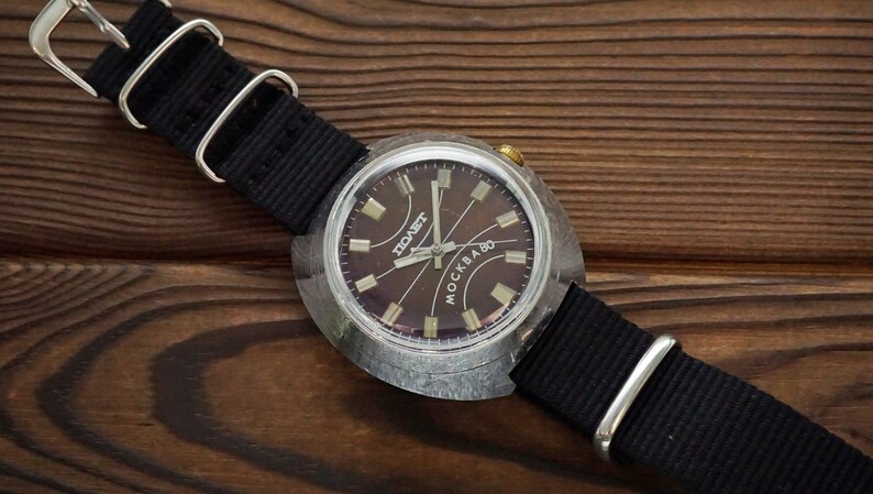 Pode incluir: Um rel&oacute;gio de pulso prateado com um mostrador preto e uma pulseira preta. O mostrador do rel&oacute;gio tem as palavras "СОВЕТ" e "МОСКВА 80" impressas nele.